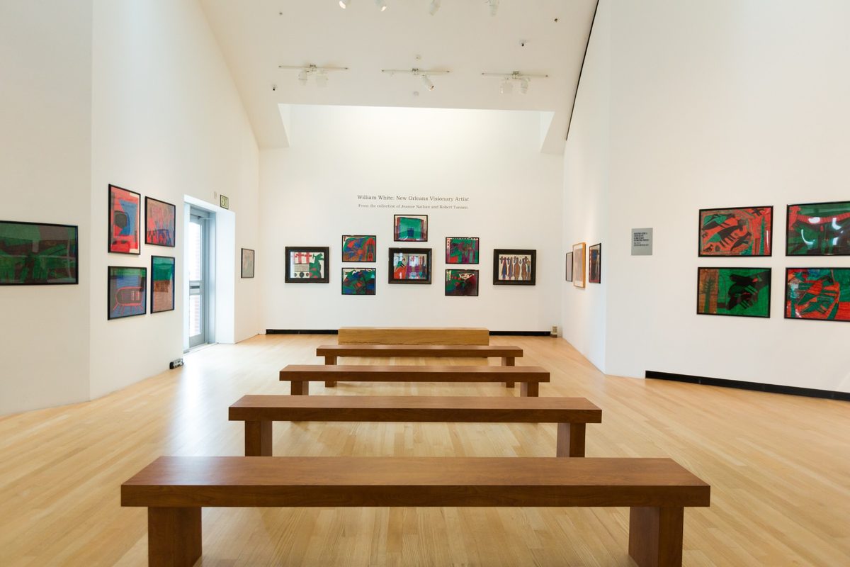 A museum gallery space includes benches and paintings on the wall.