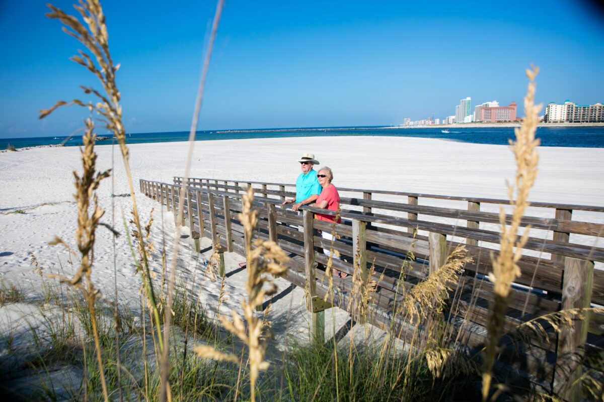 People standing on a boardwalk looking out at the ocean in Orange Beach, Alabama.