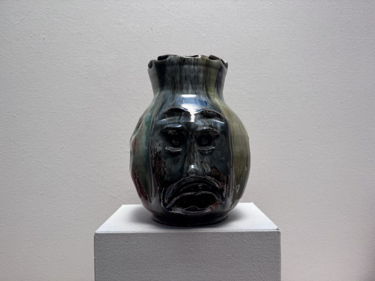 A dark green glazed vase is imprinted with a face, by ceramicist George Ohr.
